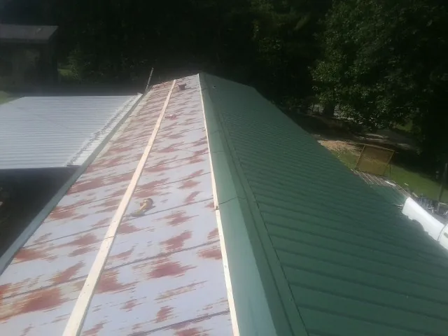 Old rusted panels beside newly installed green metal roofing — Wind Damage Roof Repair by Roofing Brothers in Lake Park