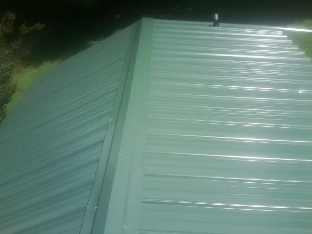 New green metal panels meeting at the ridge of a roof — Flat Roof Repair work by our crew in Lake Park