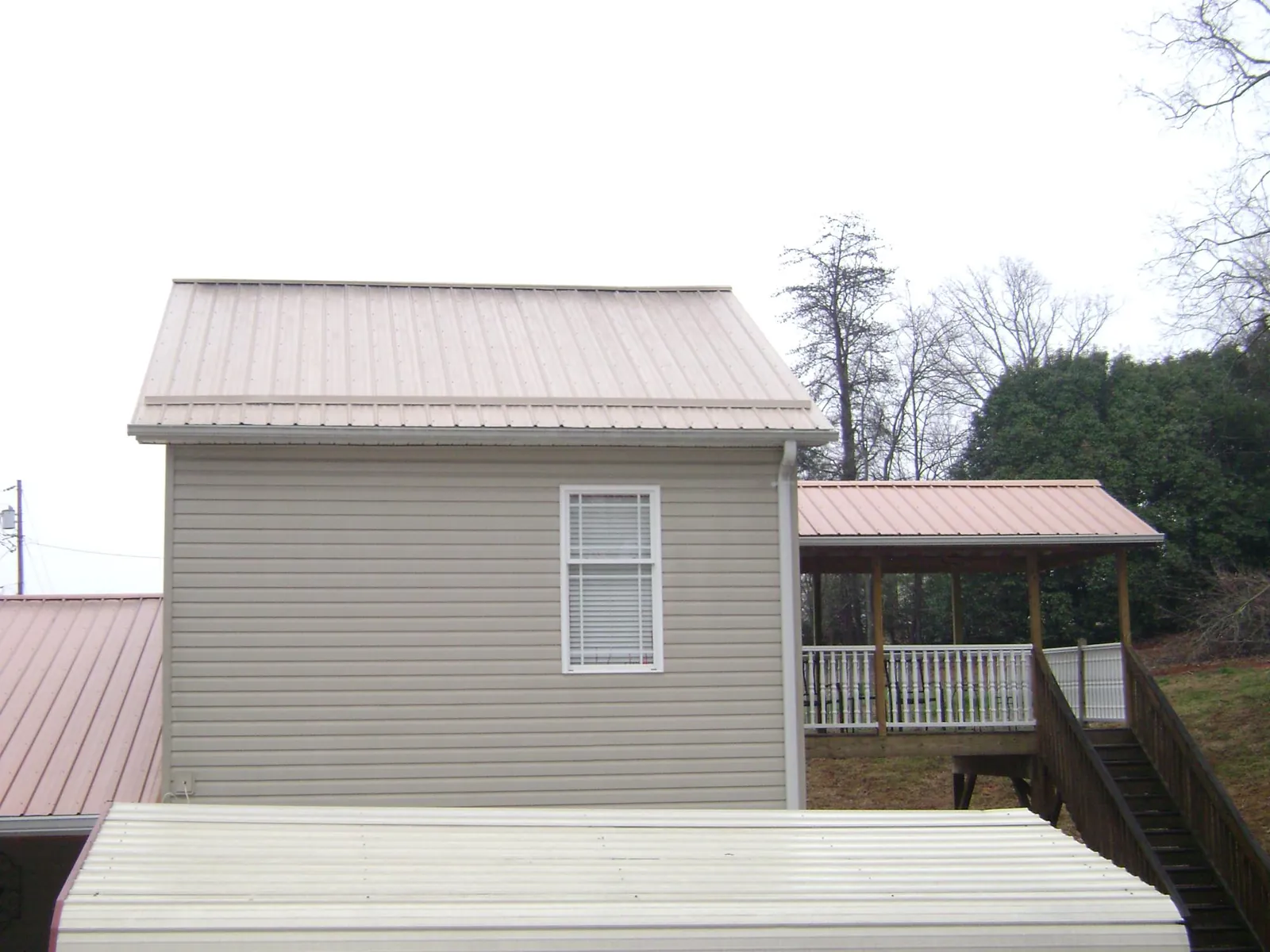 Tan metal roofs on a two story addition and attached porch, from a Roof Replacement job in Lake Park